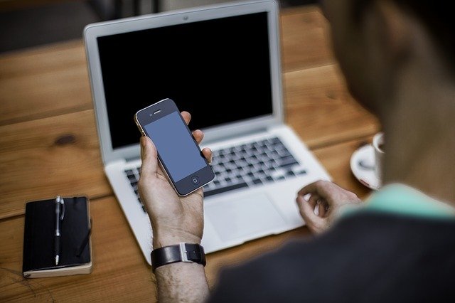 Man looking at his mobile phone with a laptop computer in the background
